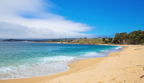 Stretch of golden sandy beach and turquoise ocean under bright blue sky