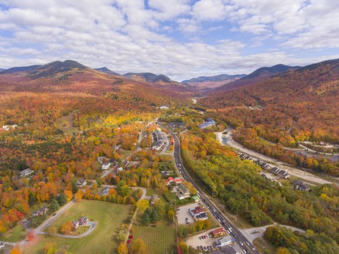 A mountainous landscape of fall trees and a road leading past a small town