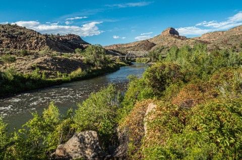 Image of river bordered by lush trees with small brown mountain in the distance.