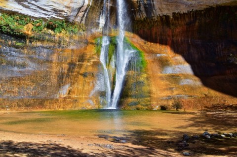 Image of thin waterfalls cascading over colorful orange and green rock formations.