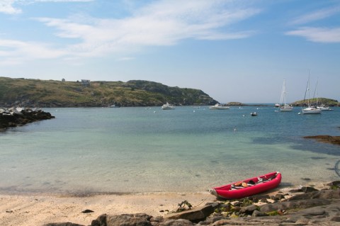 Image of calm water by beach with red boat in the foreground