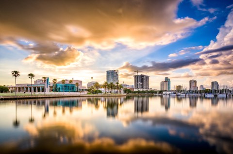 Image of city skyline of low buildings and palm trees under beautiful blue sky with golden clouds.