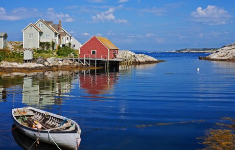 A wooden boat in a deep blue tranquil cove next to a rocky spit with a red wooden house on it