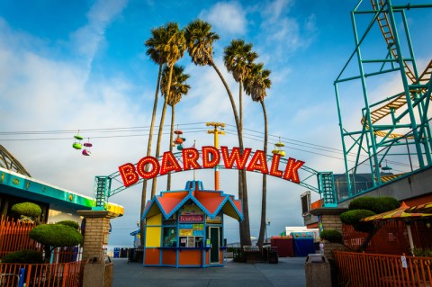 Large sign saying Boardwalk in red letters with palm trees and colorful rides.