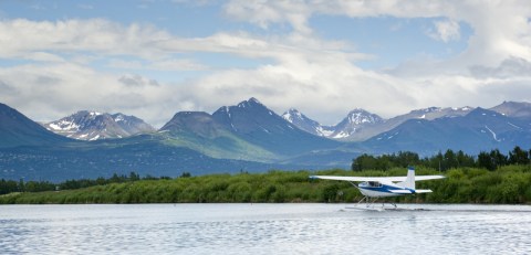 Image of small white float plane on water with snowcapped mountains in the distance.