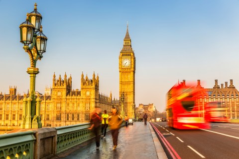 Image of people walking across a bridge at sunset with clock tower in background and red double decker bus going by