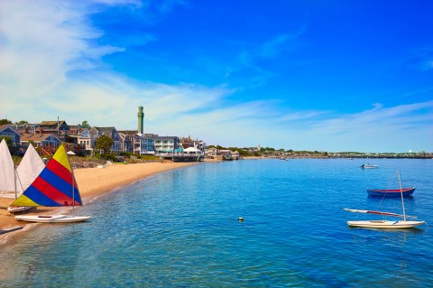 A sandy beach with colorful sailboats and charming houses under bright blue sky.