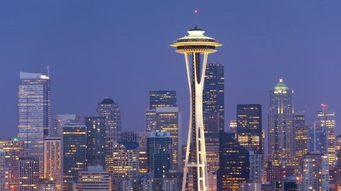 City skyline featuring the futuristic looking Space Needle lit up against purple night sky