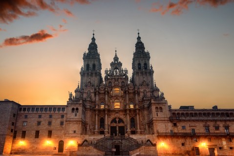 Image looking up at the facade of an ornate cathedral illuminated at sunset.