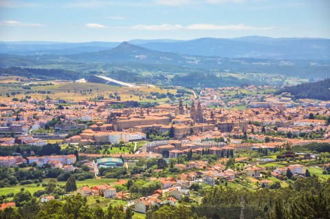 Landscape photo of a town with red roofed buildings amid rolling green hills and mountains