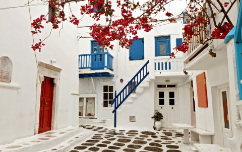 a white stone street with blue railings and pink flowers in greece