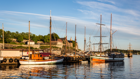 Wooden boats in a harbor with stone fortress in the background at sunset
