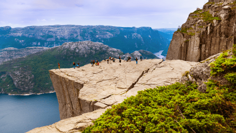 Hikers on top of flat rock cliff overlooking fjord