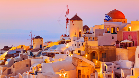 A whitewashed village and windmills on a hill under pink and orange sunset