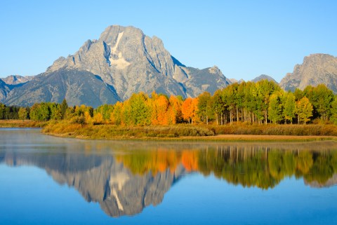 a mountain surrounded by fall foliage trees next to a lake